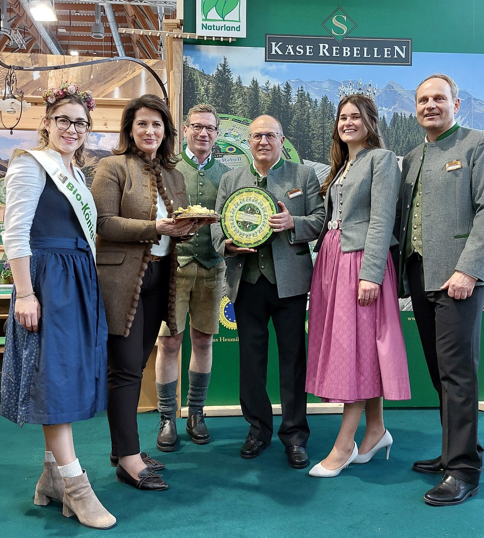 Ministerin Kaniber auf der BioFach Messe in Nürnberg bei den Käserebellen. Lachende Menschen mit Käseplatte und einem Laib Käse.