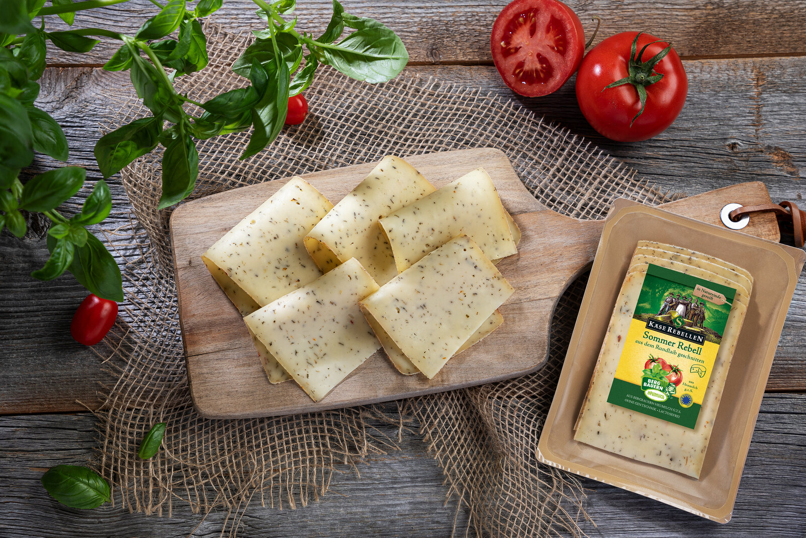 Cremiger Schnittkäse in Scheiben geschnitten auf einem urigen Holzbrett. Verziert mit Tomate und Basilikum.
