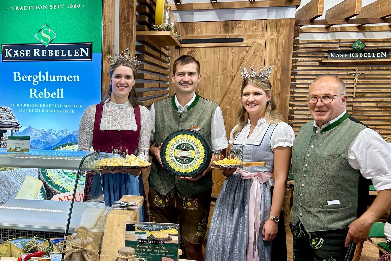 Milchkönigin und Milchprinzessin mit Andreas Krönauer. Lachende Menschen mit einem Laib Käse und Käseplatten in den Händen.