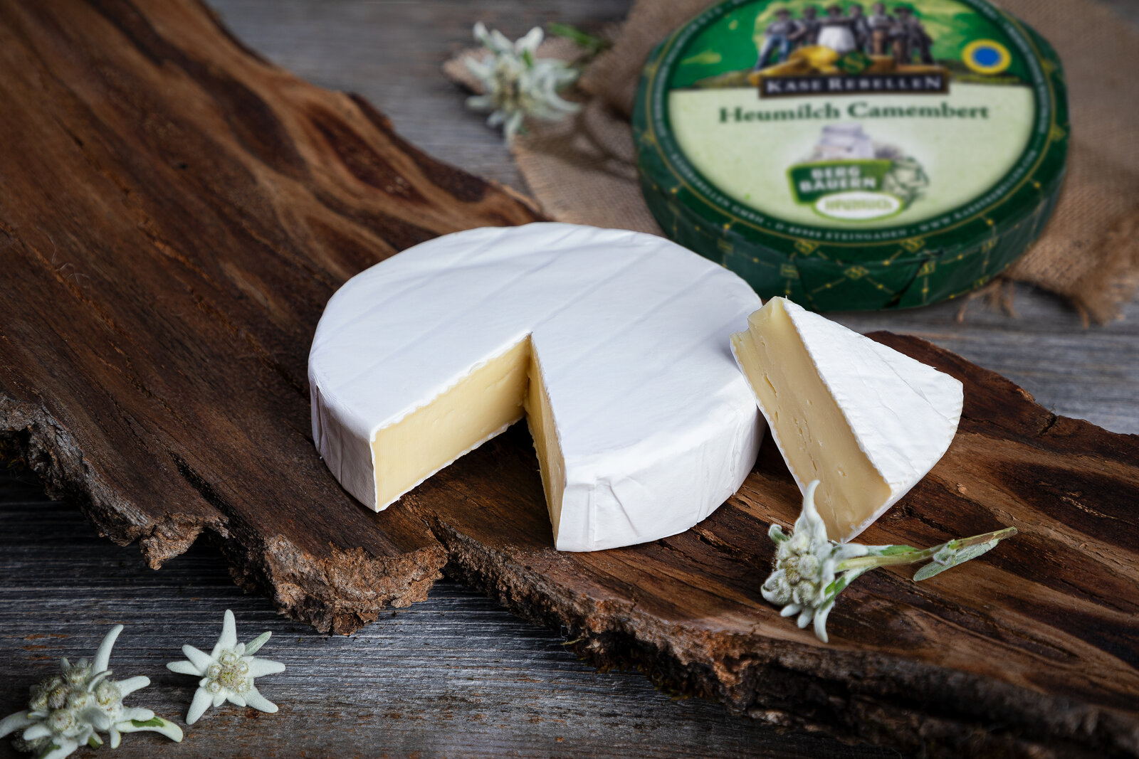 Leckerer Camembert mit einem Stück herausgeschnitten. Auf einem rustikalen Holzbrett.
