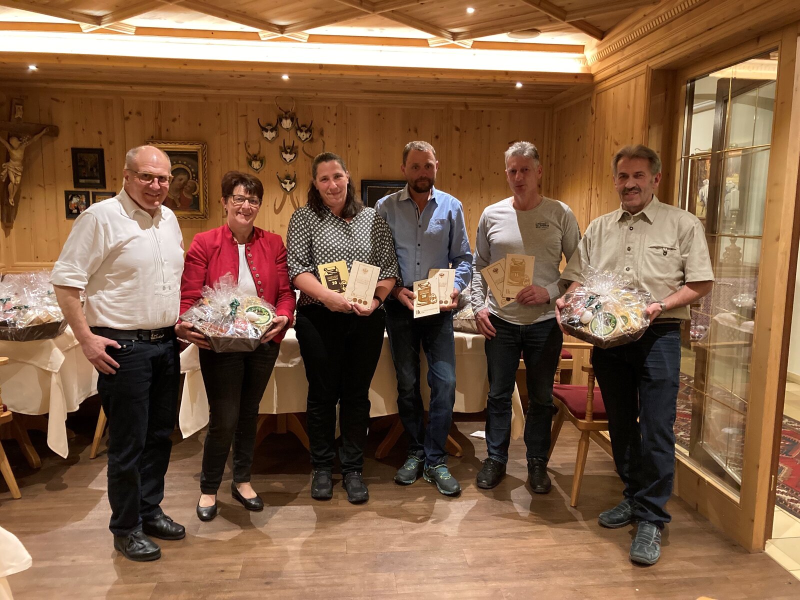 Milchversammlung Zillertal. Käserebellen auf der Milchversammlung. Lachende Menschen mit Geschenken in der Hand.